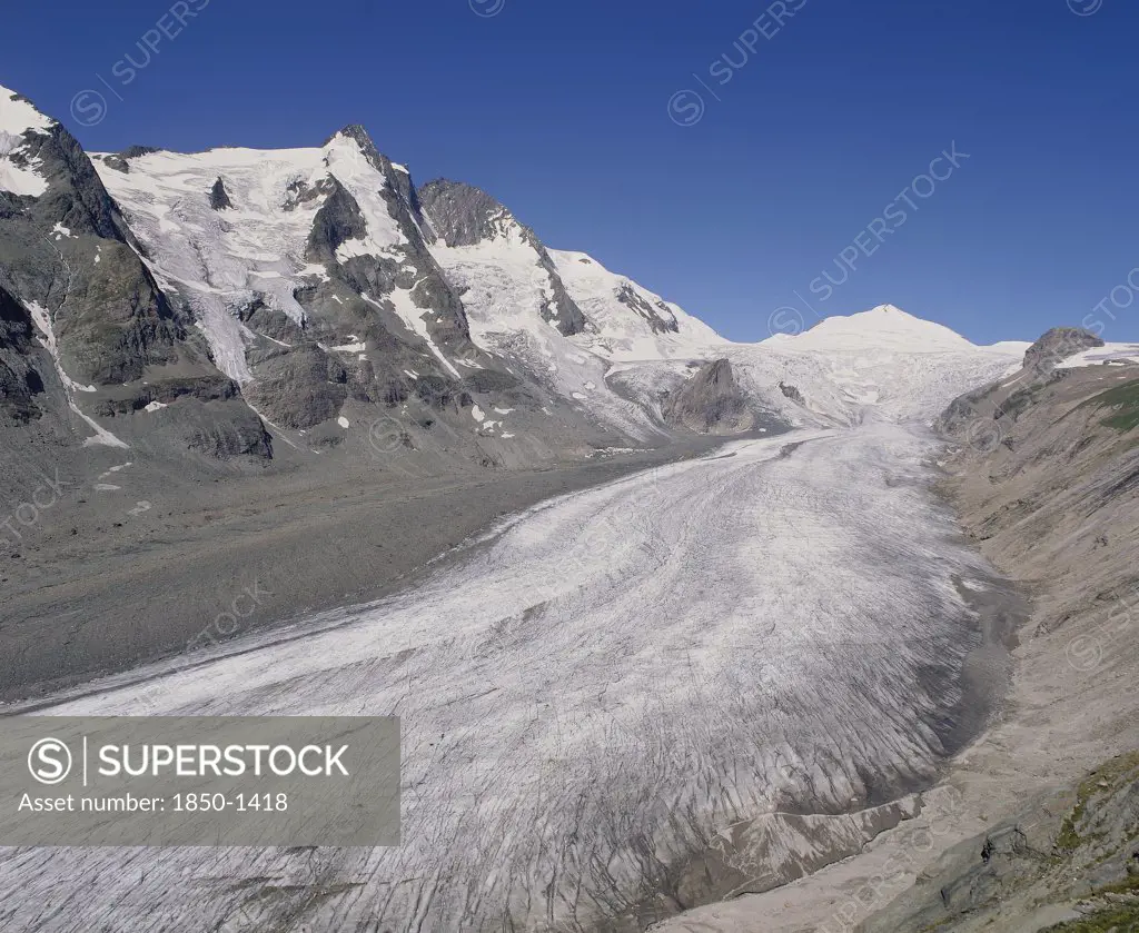 Austria, Karnten, Pasterze Glacier, View Looking Up Glacier Showing Lateral Moraine And Mountainous Sides With A Blue Sky Above