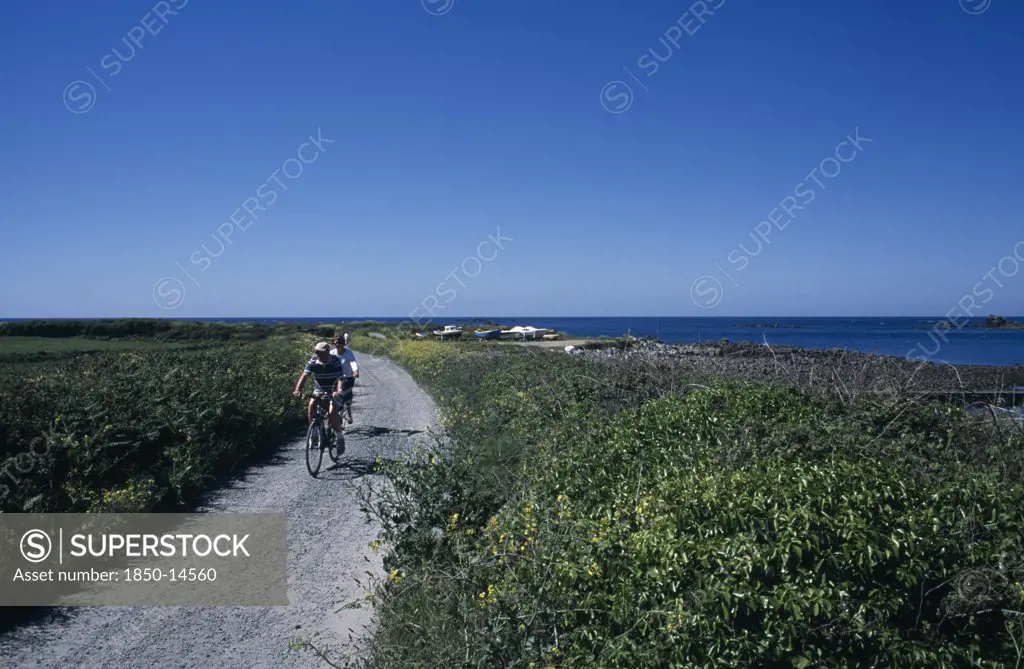United Kingdom, Channel Islands, Guernsey, Vale. Cyclists Riding On Path Next To Baie De Port Grat.