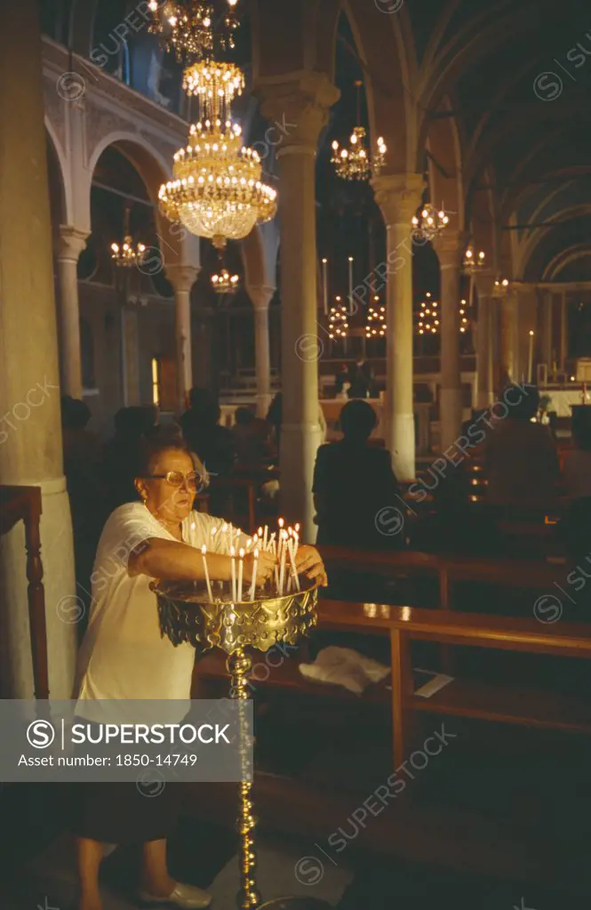 Greece, Cyclades Islands, Syros, Ermoupolis. The Interior Of The Catholic Church Of Ag. Yiorgios. Candles Being Lit And People Stood At The Pews