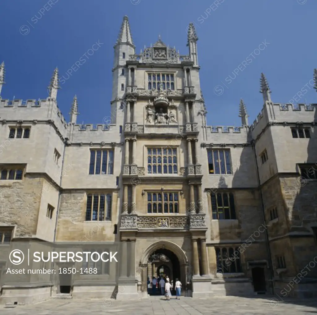 England, Oxfordshire, Oxford, The Old Bodleian Library Exterior Facade With People Walking Through Arched Entrance To Interior Courtyard.