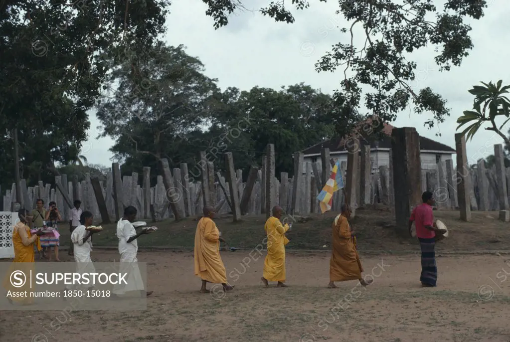 Sri Lanka, Anuradhapura, Buddhist Monks And Nuns Carrying Puja Offerings Past Columns Of The Ruins Of The Brazen Palace.