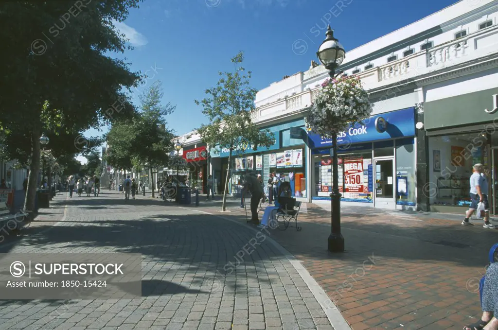 England, East Sussex, Eastbourne, Pedestrian Shopping Area With Line Of Shops And A Row Of Small Trees Casting Shadows Along The Paveing.