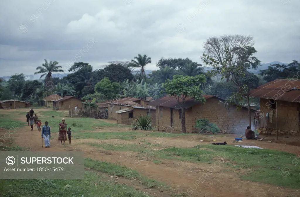 Angola, Vige, Mud Brick Village Houses With People On Unmade Road Outside.