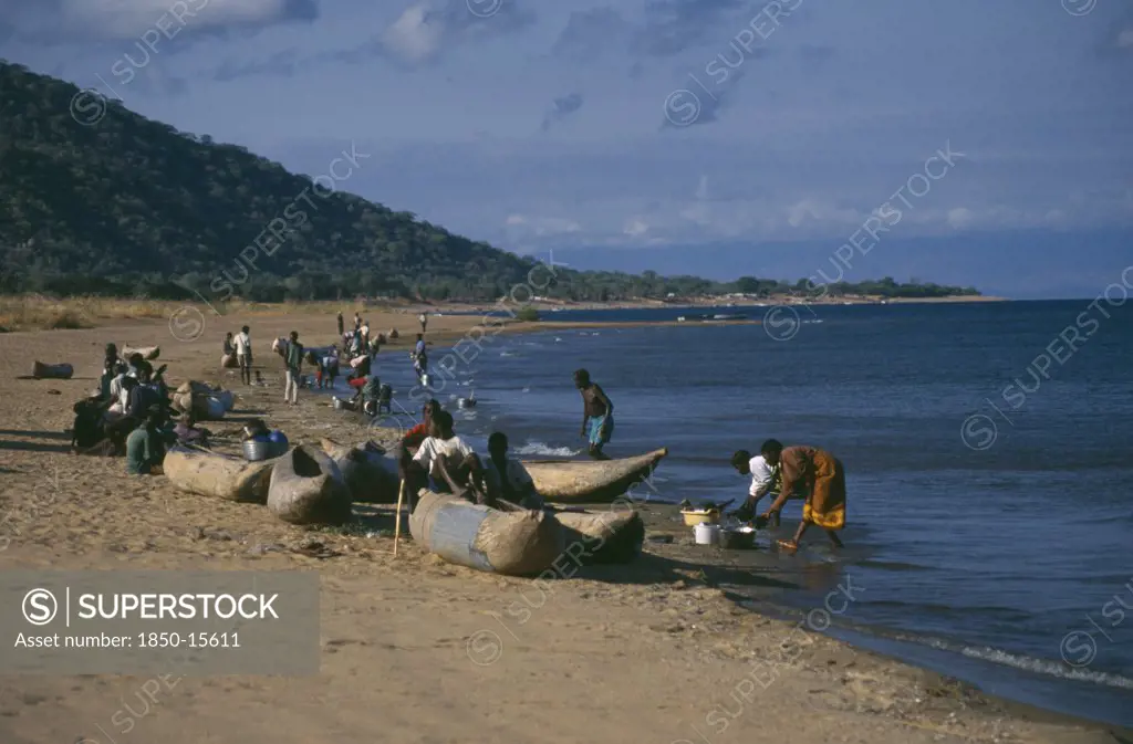 Malawi, Lake Malawi, Cape Maclear With Children Playing On Shore In Wooden Canoes And Women Washing Dishes.