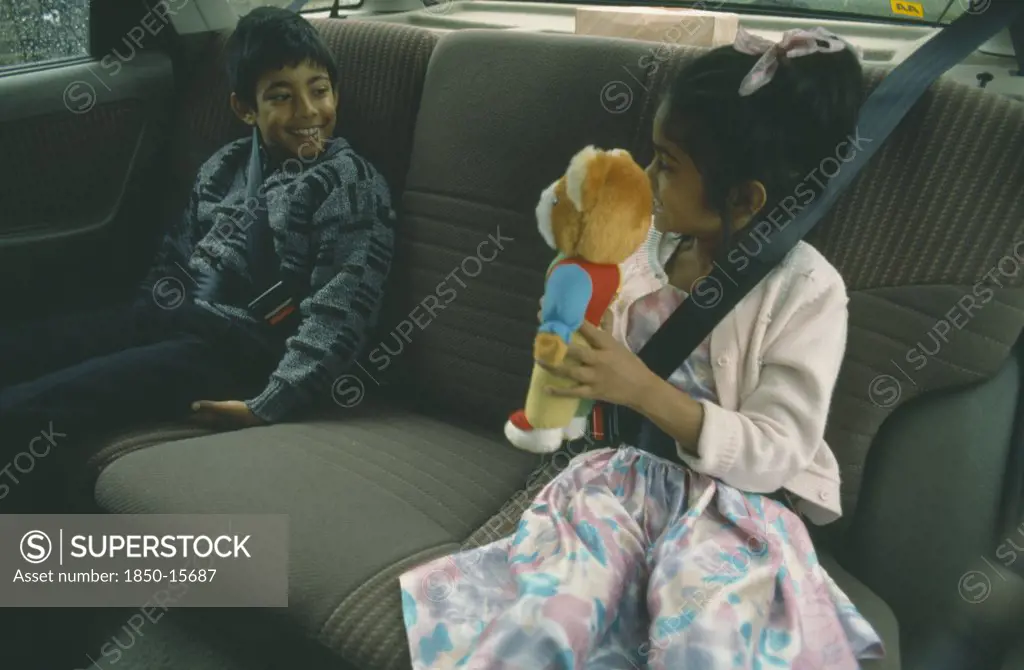England, London, Children, Two Bengali Children In Back Seat Of Car Wearing Seat Belts.  Young Girl Showing Teddy Bear To Boy.