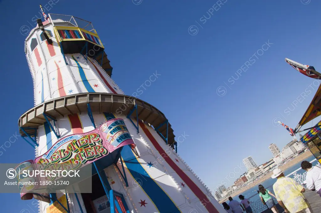 England, East Sussex, Brighton, The Helter Skelter Ride On Brighton Pier With Tourists Walking Past And The City In The Distance