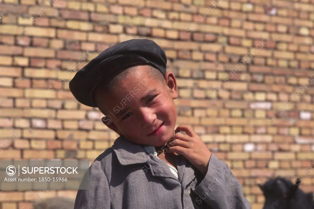 China, Xinjiang Province, Kashgar, Portrait Of Young Tajik Boy Standing In Front Of Brick Wall