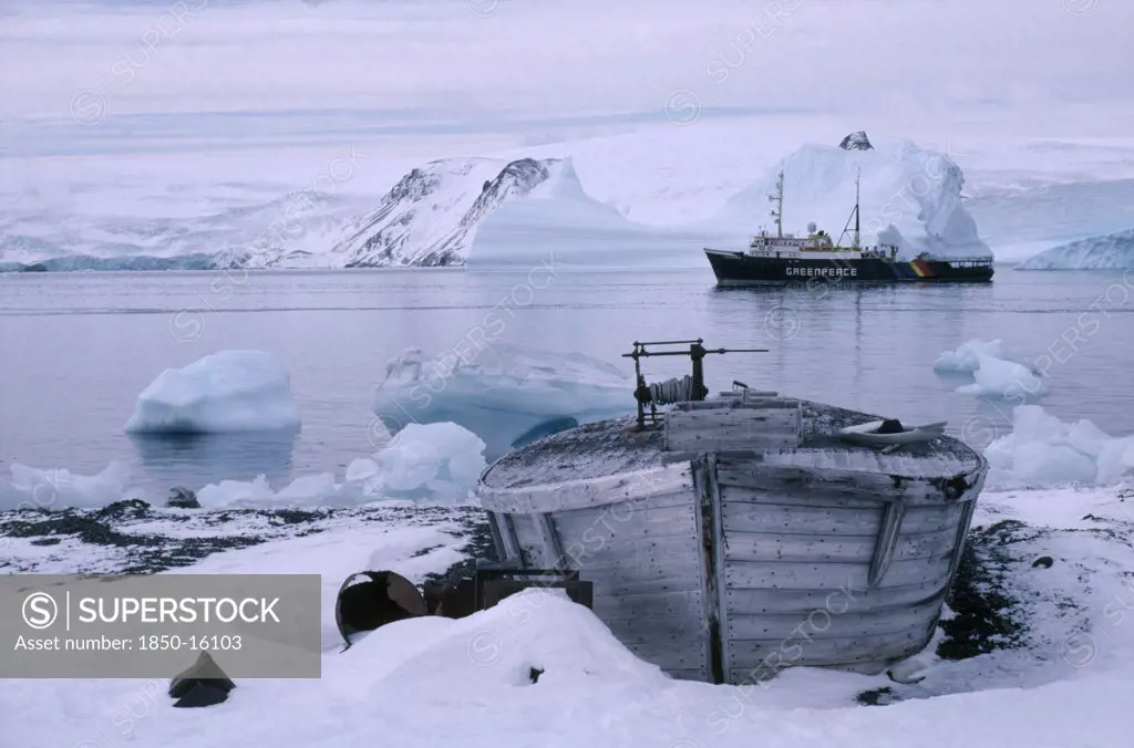 Antarctica, King George Island, Old Whale Boat On Land With Greenpeace Ship In Distance.