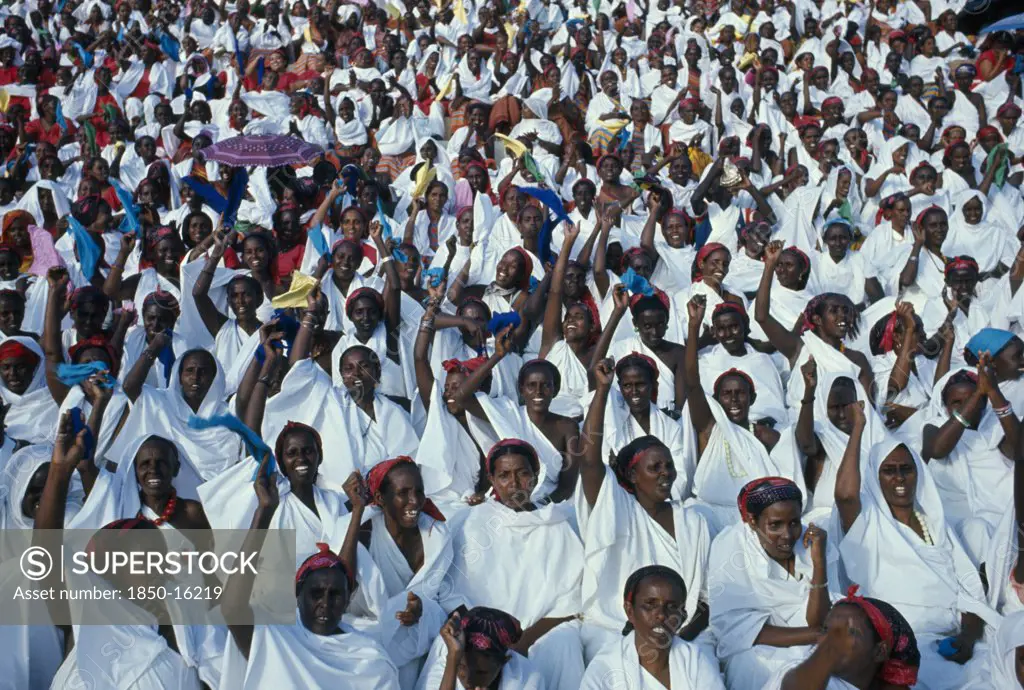 Somalia, Politics, Independence Day Parade. A Mass Of Seated Women With Their Arms Raised In The Air Dressed In White With Multi Coloured Headscarfs.
