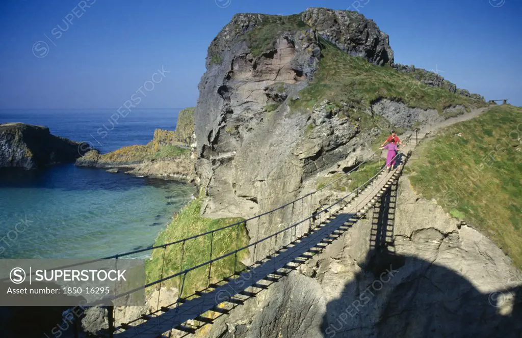 Ireland, County Antrim, Carrickarede, Visitors Crossing Narrow Rope Bridge On The Irish Coast.