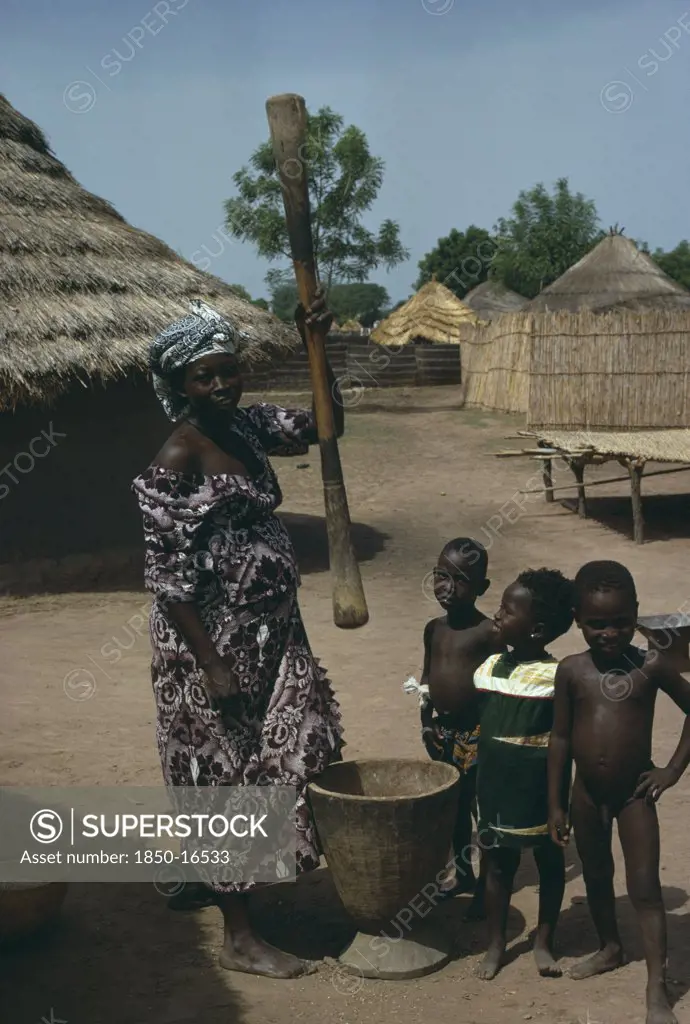 Gambia, Agriculture, Woman Pounding Grain In Village With Children Gathered Around Her