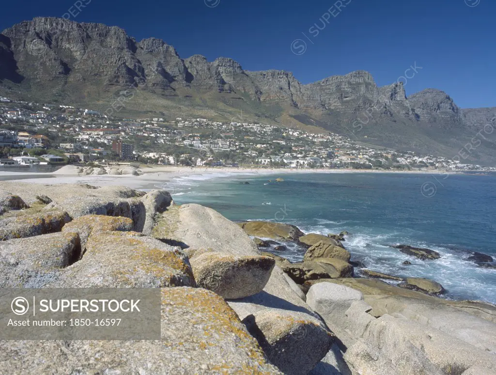 South Africa, Western Cape, Cape Penninsula, View Across Rocks Towards Clifton Bay And Beach.  Hillside Buildings With The Twelve Apostles Behind