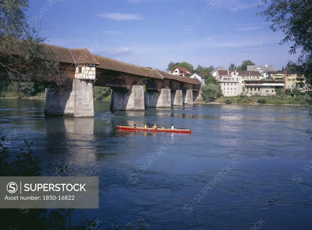 Germany, Baden Wurttemberg, Covered Wooden Bridge Over The Rhine Which Links Badsackingen With The Stein In Switzerland. People In Row Boat.