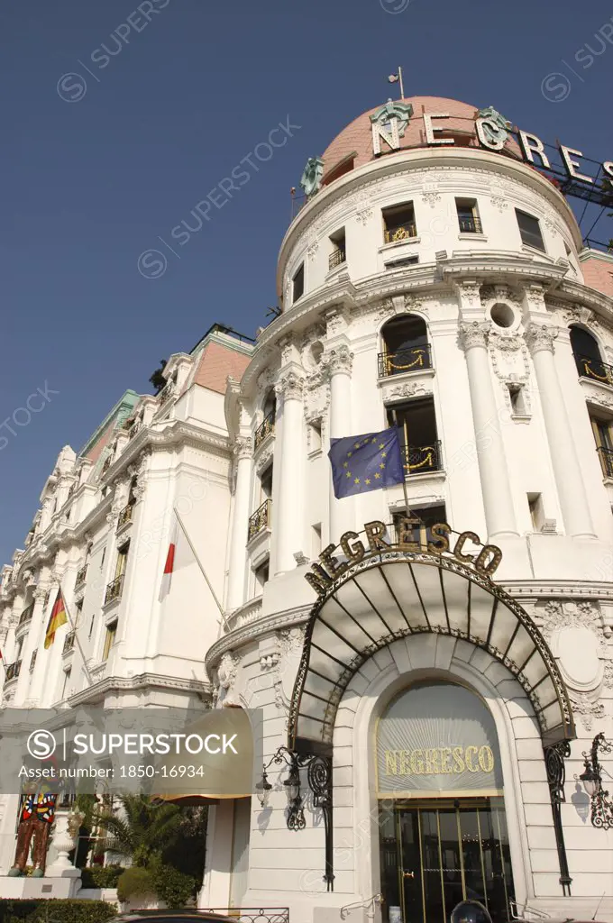 France, Nice, Negresco Hotel, 'The Entrance With Sign, European Union, German And Japan Flags Flying. Statue Of Man Playing Saxophone.'