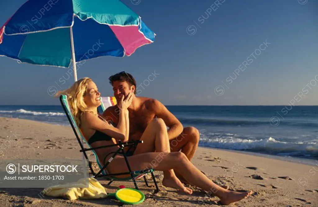 Usa, Florida, Fort Lauderdale, Young Couple On Sandy Beach Sitting Under A Parasol