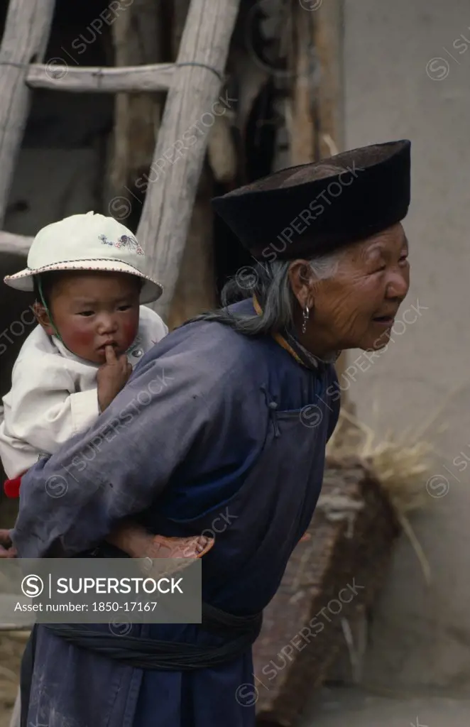 China, Qinghai Province, Huzhu District, Elderly Tu Nationality Lamaist Woman Of Yellow Hat Buddist Sect Carrying Child On Her Back.