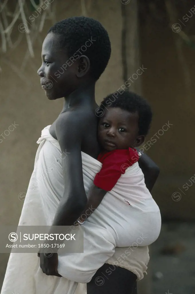 Ghana, Children, Child Carrying Sibling On Her Back Wrapped In White Cotton Cloth.