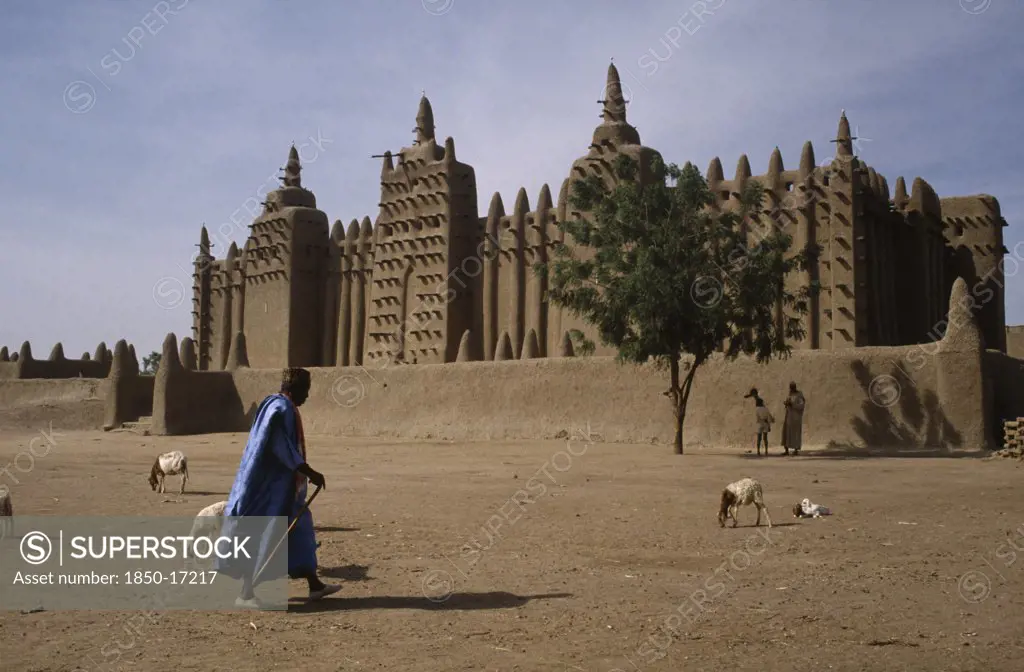 Mali, Sahel, Djenne, Grand Mosque With Man Walking Past And Sheep In The Foreground.