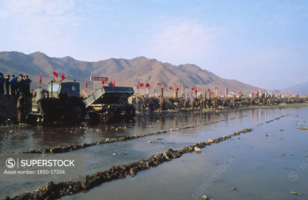 North Korea, North Hwanghhae Province, Pyongsan County, Juche People In A Line Reparing Flood Dykes With Red Flags Fyling And Mountains Behind Them