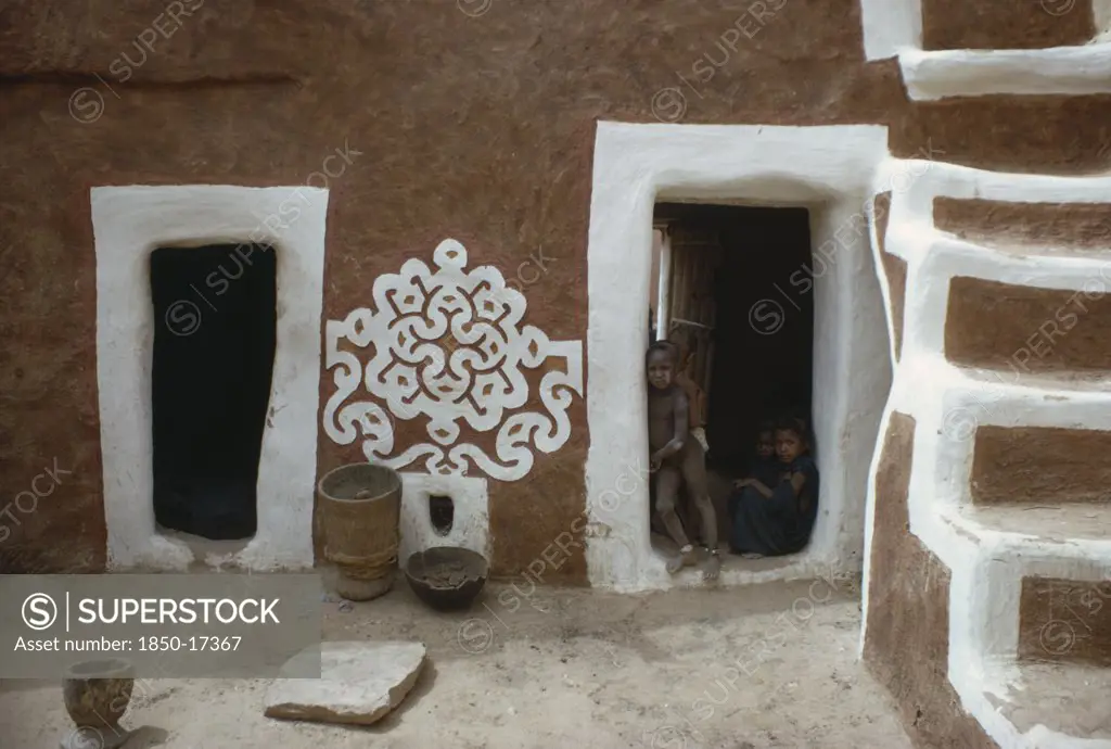 Mauritania, Oualata, Traditional Mud Architecture Decorated With Bas Relief Motif Of Applied Gypsum  White And Red Clay.  Children Framed In Open Doorway With White Surround.