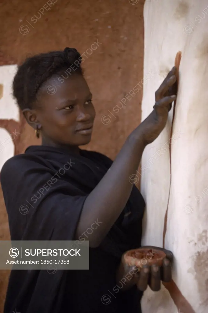 Mauritania, Oualata, Young Woman Decorating Exterior Wall Of Mud Building With Ochre.  It Is Traditional For Women To Both Design And Apply Such Decorations.