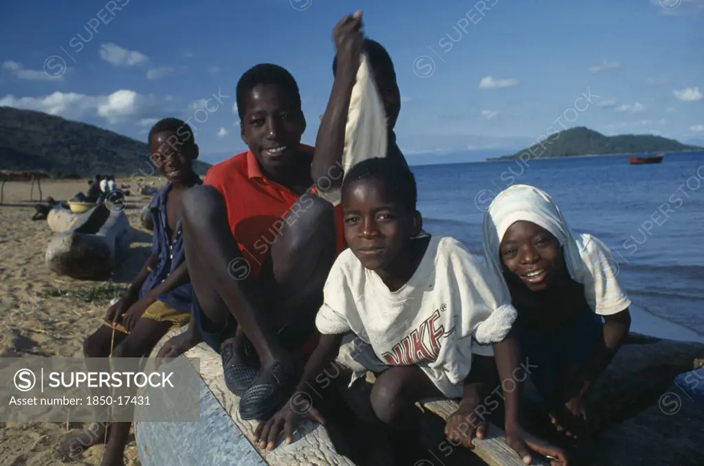 Malawi, Cape Maclean, Lake Malawi, Group Of Children Sitting On Boat On Lake Shore.