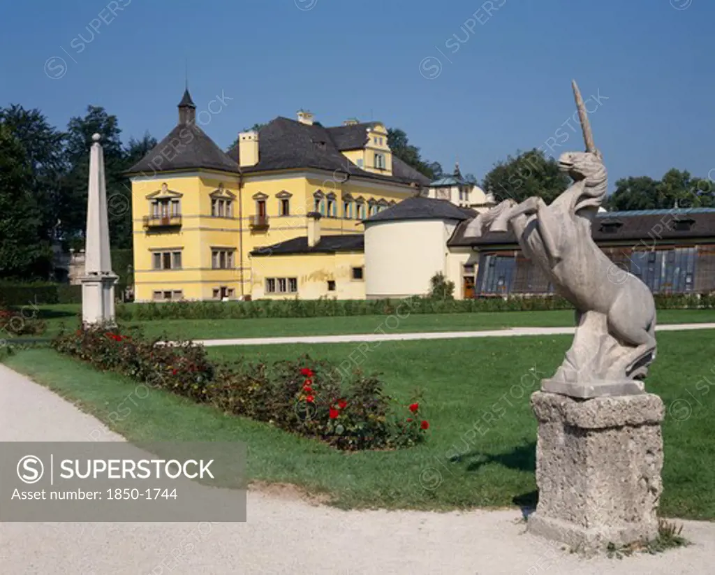 Austria, Salzburg Province, Salzburg, 'Hellbrunn Palace, Yellow Building Seen From Across Gardens With A Unicorn Statue In The Foreground'