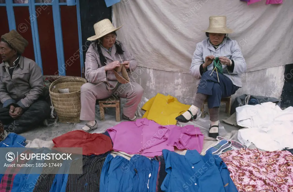 Tibet, Lhasa, Women Vendors Knitting At Clothing Stall In Street Market Near The Jokhang Monastery.