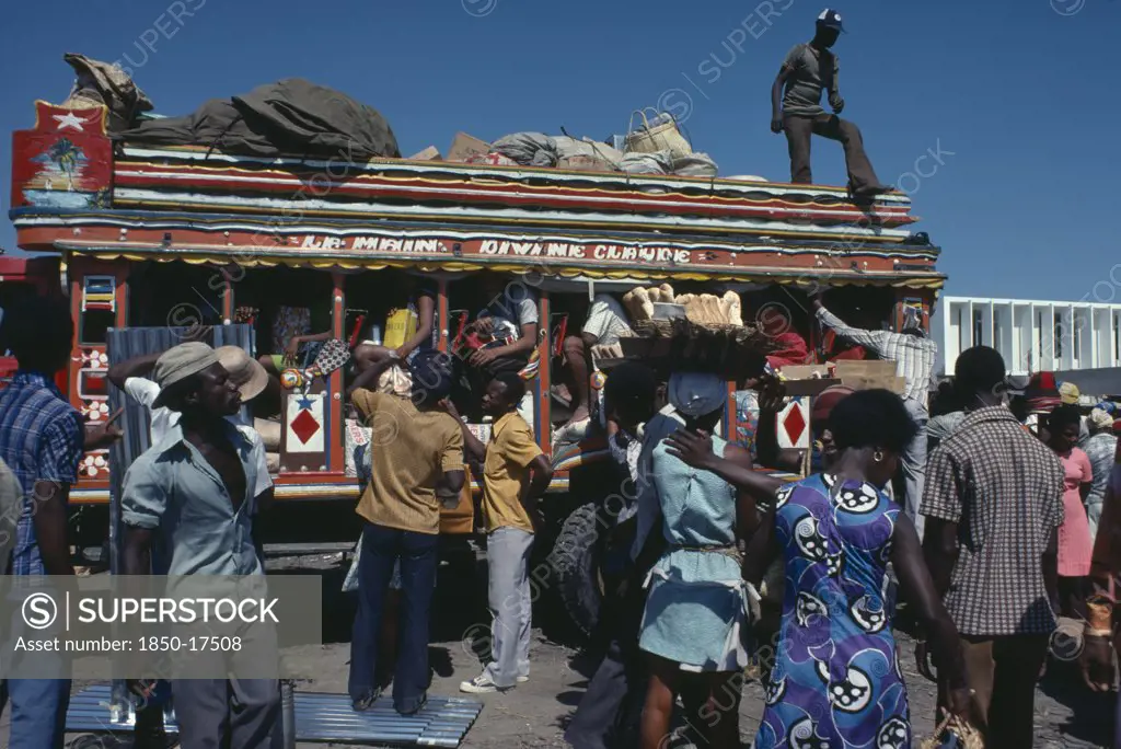Haiti, Transport, Brightly Painted And Crowded Taptap Bus With Waiting Crowds And Food Sellers.