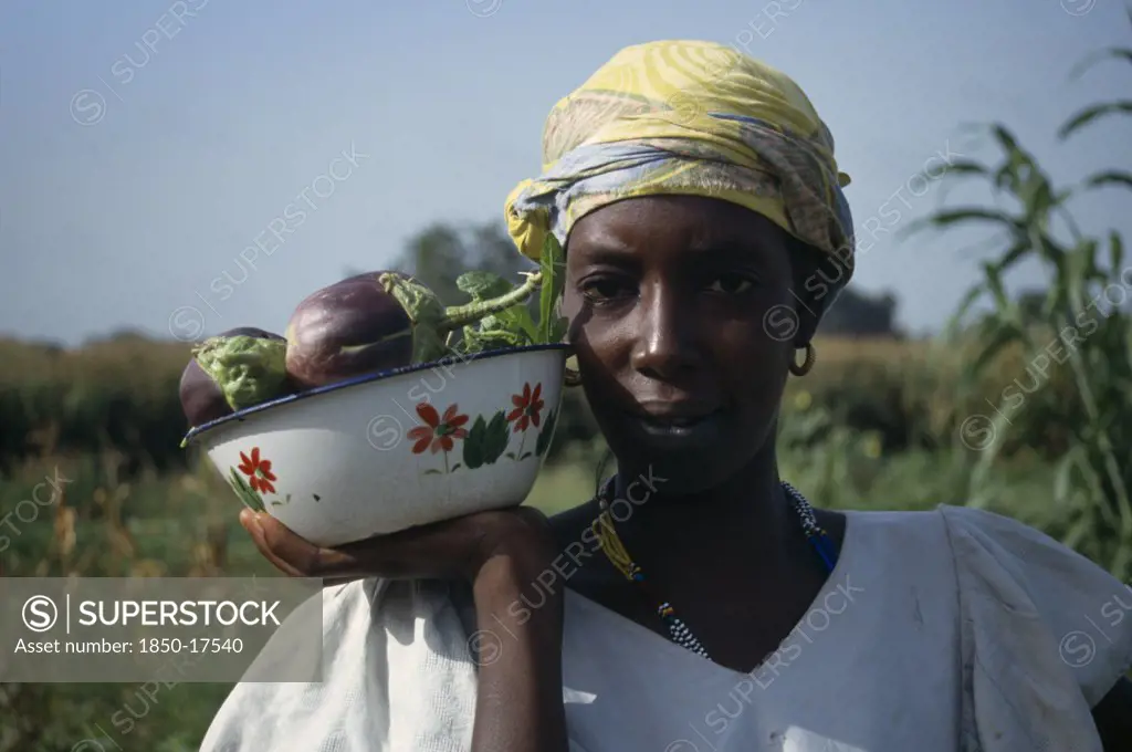 Gambia, Agriculture, Head And Shoulders Portrait Of Woman Holding Dish Of Aubergines.
