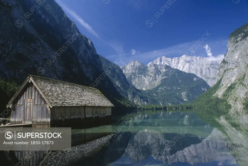 Germany, Berchtesgaden, Konigssee, A Boathouse Amidst Tranquil Water On The Far Side Of The Obersee.