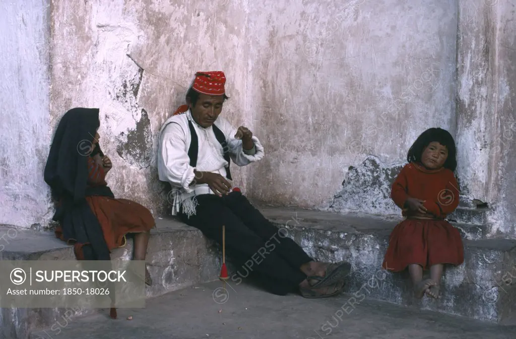 Peru, Puno, Lake Titicaca, Taquile Man Spinning Wool With His Two Children Sitting Either Side Of Him.