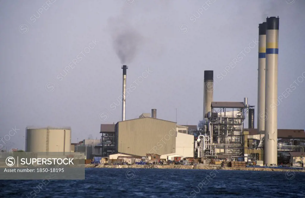 Curacao, Willemstad, Seawater Desalination Plant Exterior With Narrow Chimney Emitting Black Smoke.