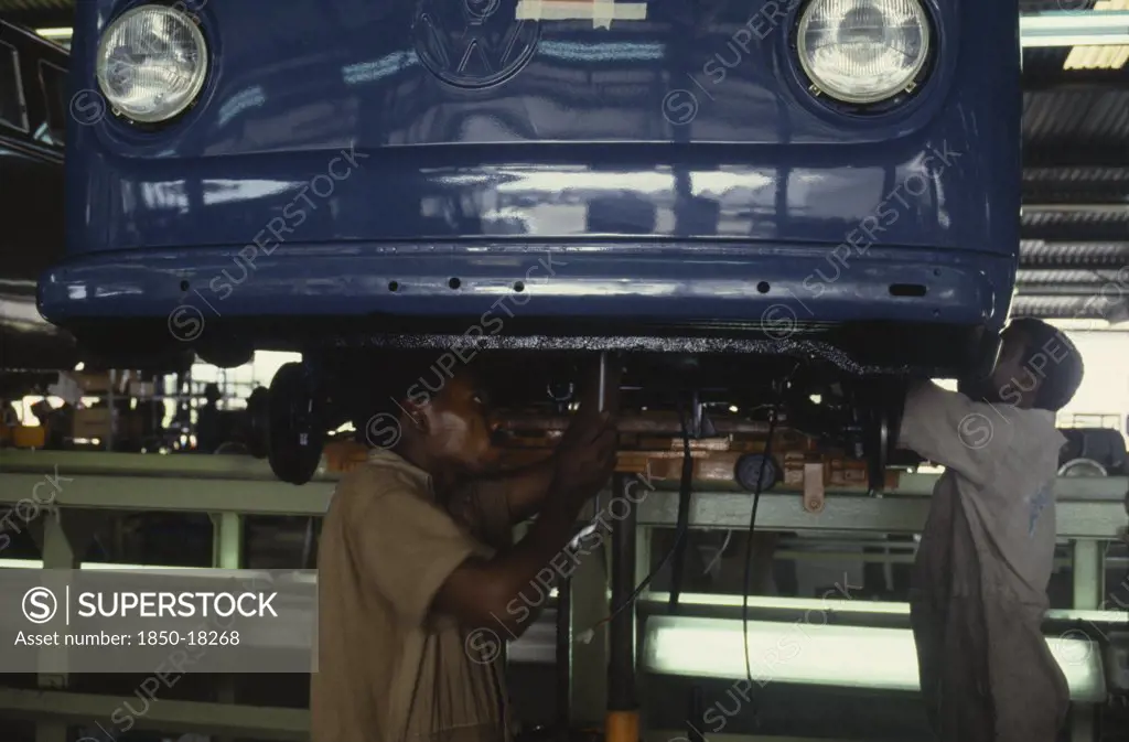 Nigeria, Lagos, Men Working On Underside Of Car On Volkswagen Car Assembly Line.