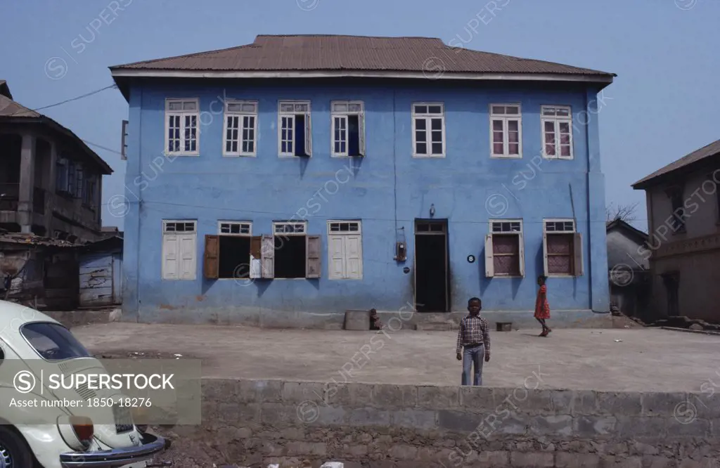 Nigeria, Inagbiji, Blue Painted Exterior Of Typical House With Wooden Shutters And Children In Yard Outside.
