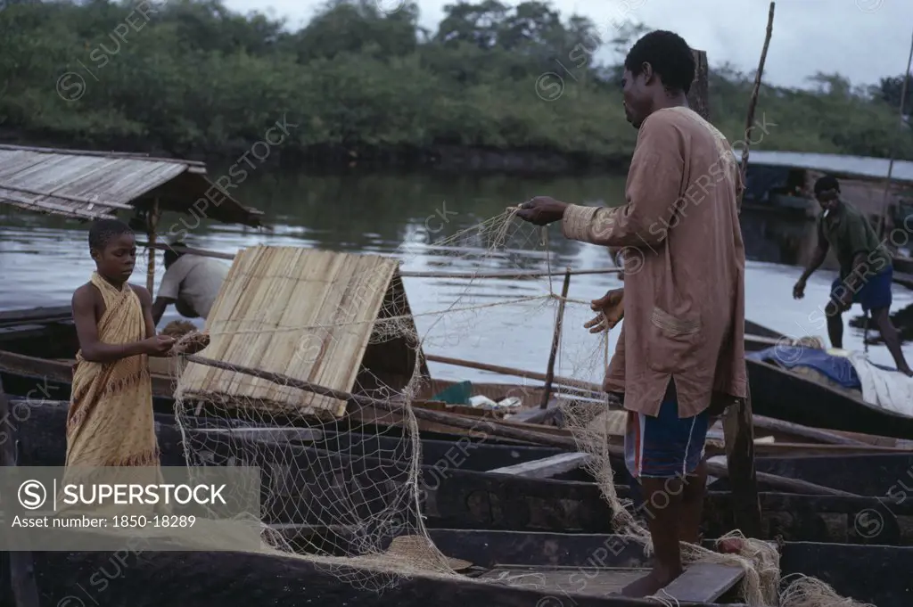 Nigeria, Bonny, Fisherman And Young Girl Untangling Nets In Wooden Canoes.