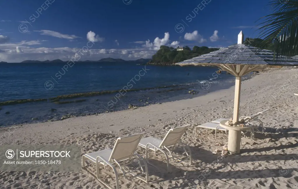 Grenadines, Mustique, Endeavour Bay. Empty Sun Loungers On Sandy Beach With Bequia Island Seen From Across The Sea In The Distance