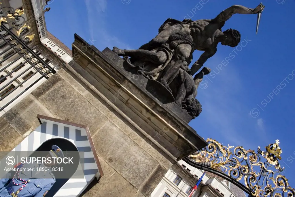 Czech Republic, Bohemia, Prague, Soldier Standing Guard At A Sentry Box Below An 18Th Century Statue Of Fighting Giants By Ignaz Platzer At The Entrance To Prague Castle In Hradcany