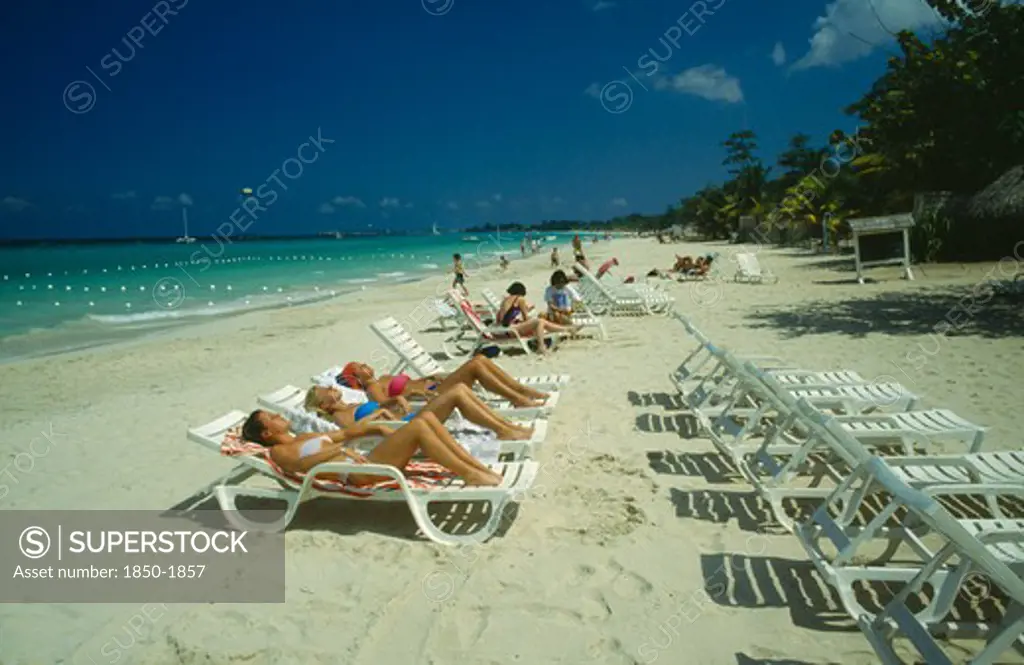 West Indies,  Jamaica, Negril, Female Tourists Beach Sunbathing On Sun Loungers Facing Away From The Water