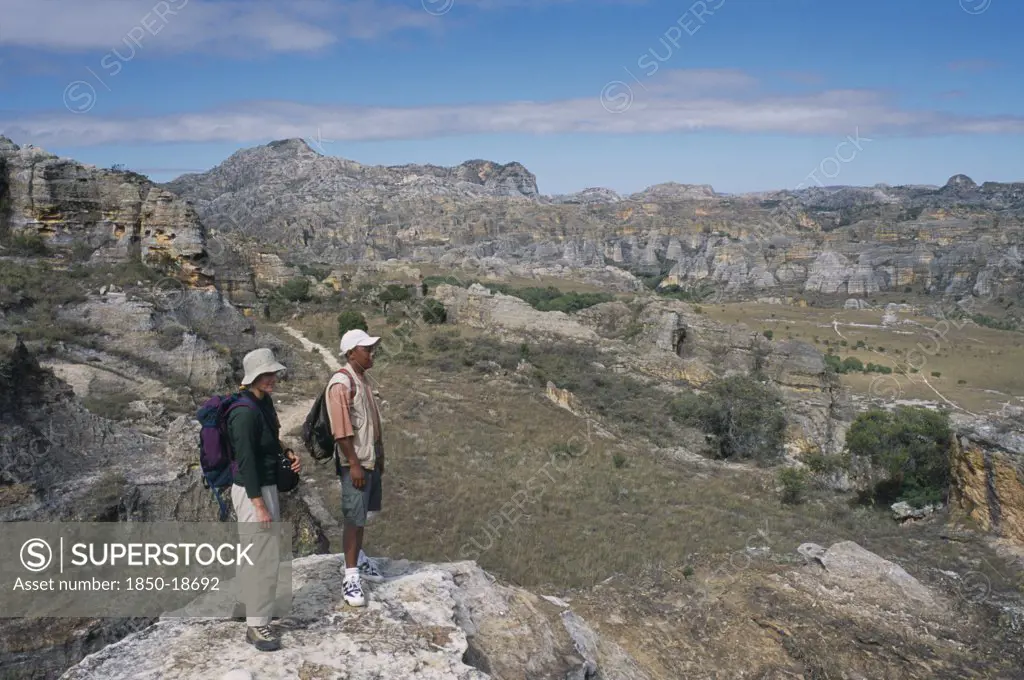 Madagascar, Isalo National Park, Tourist And Guide Standing On Edge Of Rock Looking Over Craggy Sandstone Massifs