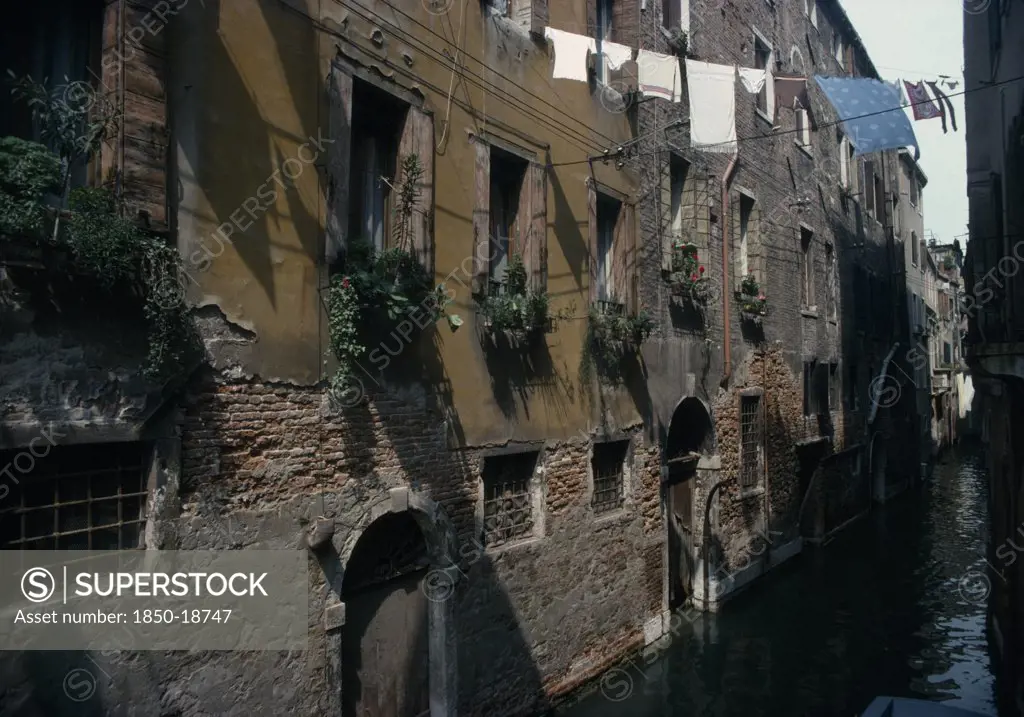 Italy, Veneto, Venice, 'Canalside Houses With Crumbling Plaster And Brickwork, Plants And Flowers In Window Boxes And Washing Hanging Between Buildings Overhead.'