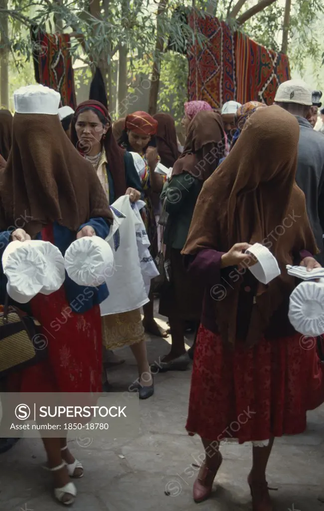 China, Xinjiang, Kashgar, Veiled Women Selling Hats Amongst The Crowd At The Sunday Market.