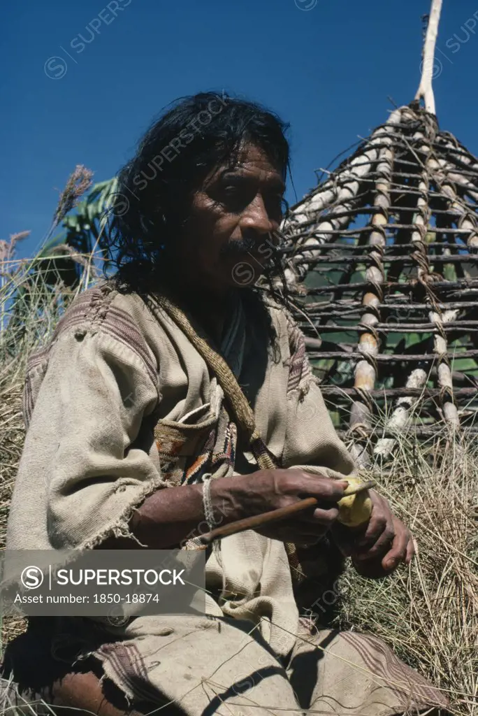 Colombia, Sierra Nevada De Santa Marta, San Antonio, 'Mama/Priest Valencia Takes A ''Coca Break'' - Taking Lime Powder From His Poporo/Gourd To Put Into Wad Of Coca Leaves In His Mouth - Whilst Thatching The Roof Of His House Wearing Traditional Thick Woven Cotton Manta/Cloak Indigenous Tribes American Northern Caribbean Slopes Of Sierra  '