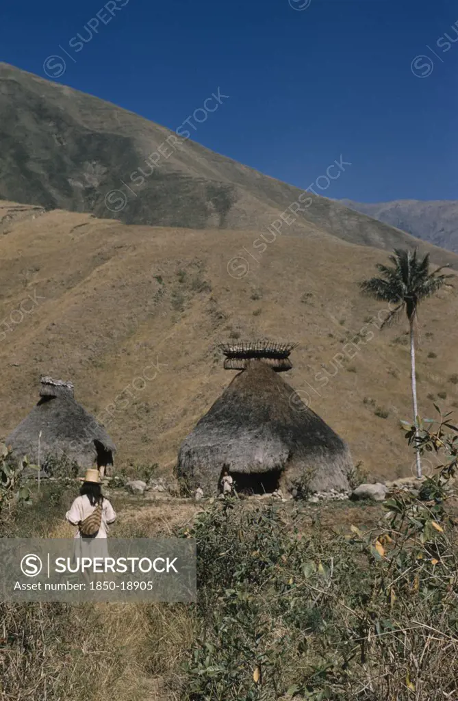Colombia, Sierra Nevada De Santa Marta, Kogi Tribe, 'Religious Centre Of Takina, High In Sierra Nevada. Man Wearing Hand Woven And Hand Dyed Mochila / Shoulder Bag, Walks To Meet A Mama / Priest Emerging From The Nuhue / Temple, With Large Rack Of Potsherds At The Roof Apex'