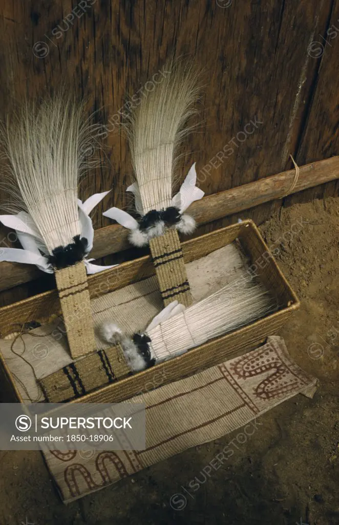 Colombia, Vaupes Region, Tukano Tribe, 'Sacred Box Of Ceremonial Feather Head-Dresses, Ritual Adornments, Hung From Maloca Longhouse Roof And Brought Down Only For Festivals /Dances. Royal Crane Tail Feather Headdress, Dyed Bark-Cloth Apron In Foreground'