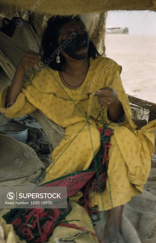 Colombia, Guajira Peninsula, Guajiro / Wayuu Tribe, 'Woman Embroiders A Faja / Woven Woollen Belt For Her Husband, Sitting On A Fique / Cactus Fibre Hammock; Face Smeared With Black Fungal Paint Mixed With Goat Fat.'