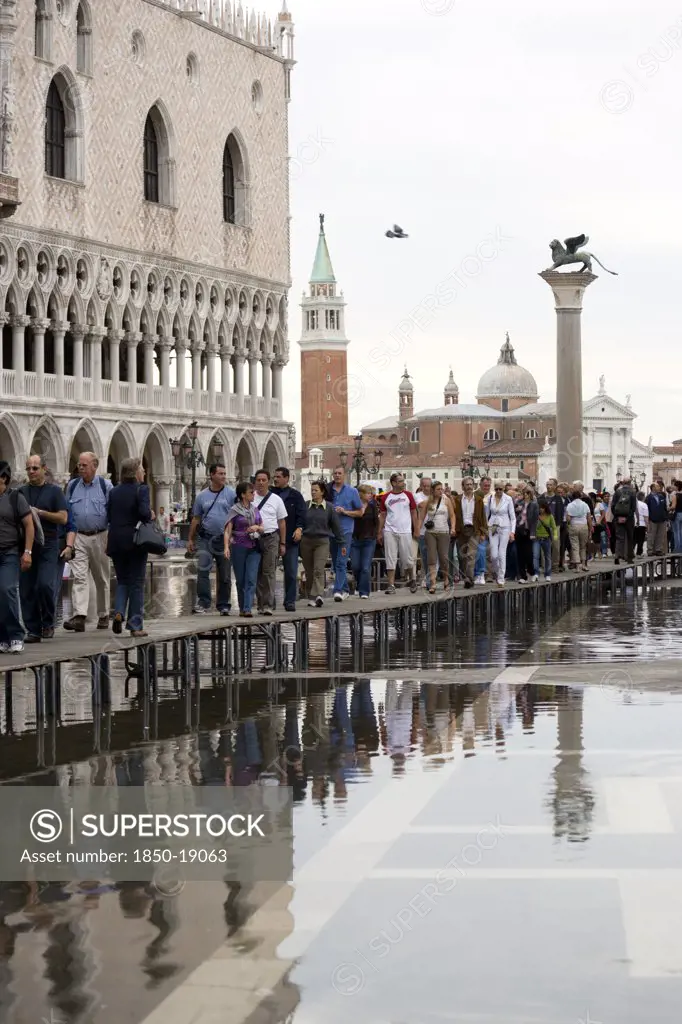 Italy, Veneto, Venice, Aqua Alta High Water Flooding In St Marks Square With Tourists Walking On Elevated Walkways Outside The Doges Palace