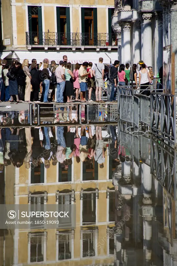 Italy, Veneto, Venice, Aqua Alta High Water Flooding In St Marks Square With Tourists Queuing On Elevated Walkways To Enter St Marks Basilica