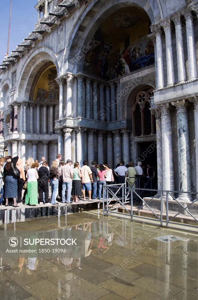 Italy, Veneto, Venice, Aqua Alta High Water Flooding In St Marks Square With Tourists Queuing On Elevated Walkways To Enter St Marks Basilic