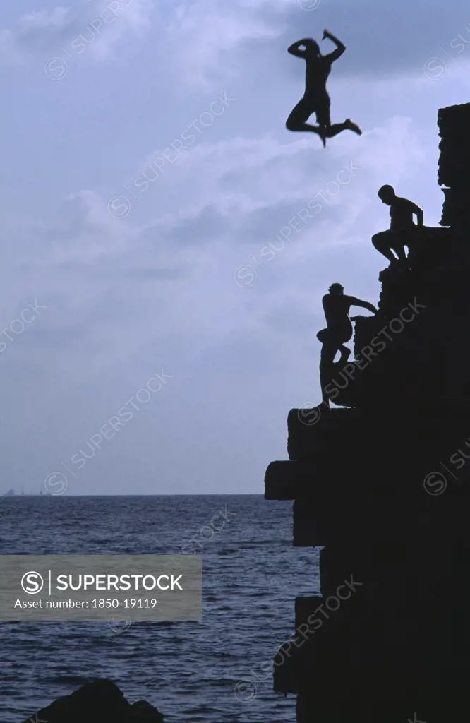 Israel, Acre, Arab Boys Climbing The Old Harbour Walls To Jump Into The Sea With A Boy Leaping Into The Air At The Top